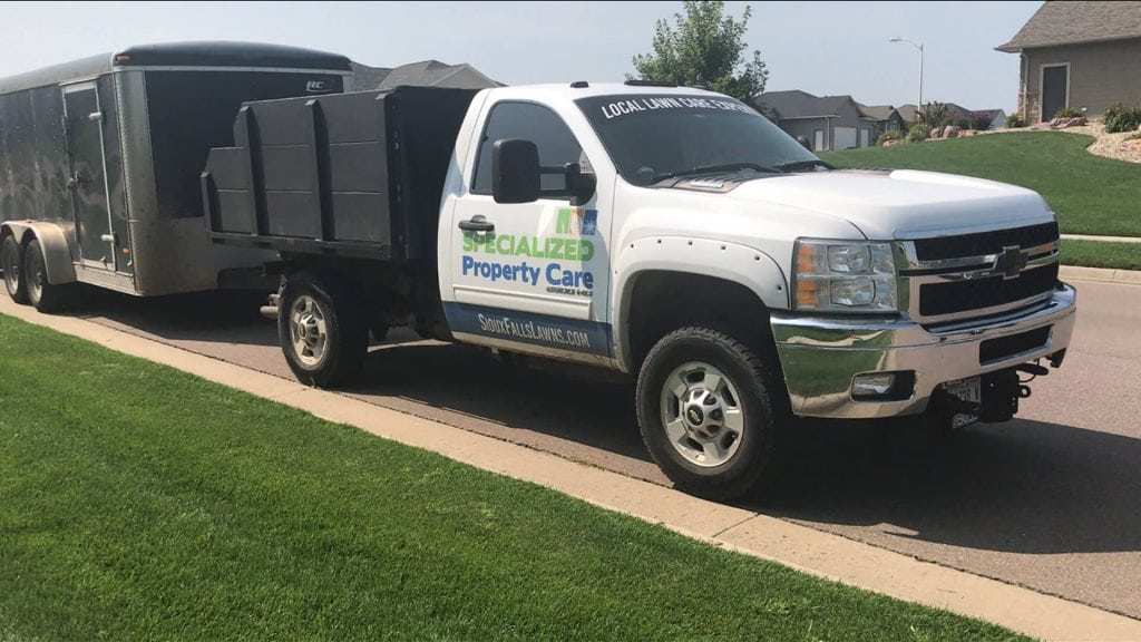 White truck with "Specialized Property Care" branding, parked on residential street, adjacent to a black trailer, showcasing lawn care service vehicle in Sioux Falls.