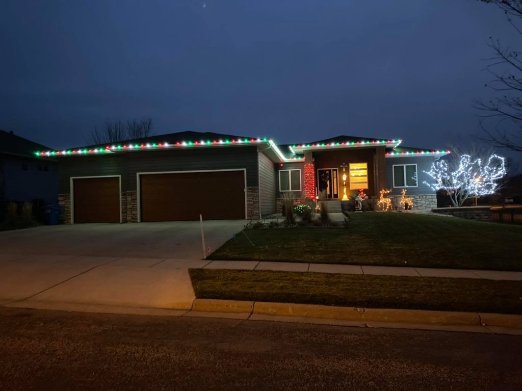 Residential home decorated with holiday lighting, featuring colorful lights along the roof, illuminated trees, and festive decorations, showcasing Specialized Property Care's holiday lighting services for enhanced curb appeal.