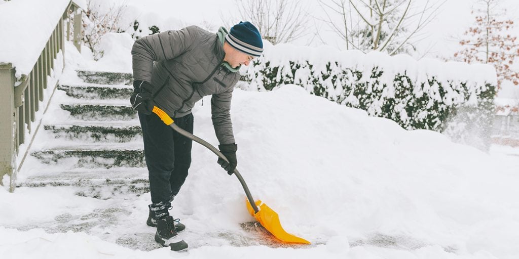 Person shoveling snow from a residential walkway, emphasizing snow removal services by Specialized Property Care for safe winter access.