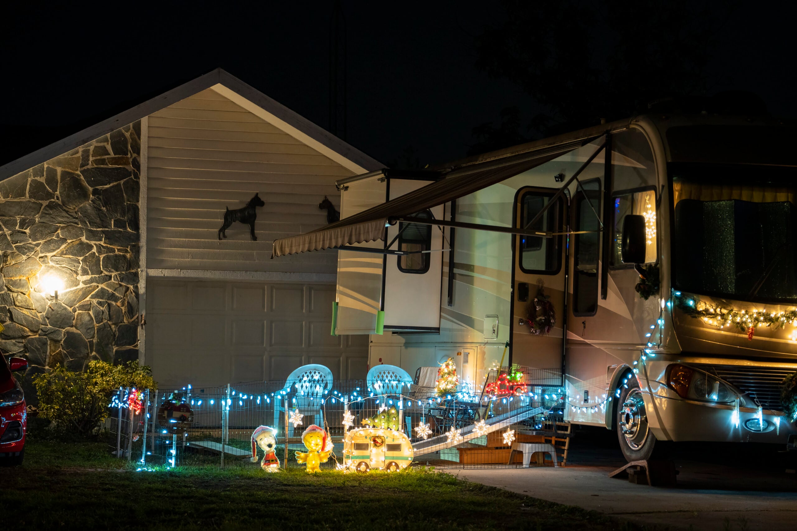 Outdoor holiday lighting installation on a residential property featuring illuminated decorations, a festive RV adorned with lights, and cheerful light-up characters, creating a warm and inviting atmosphere for the holiday season.